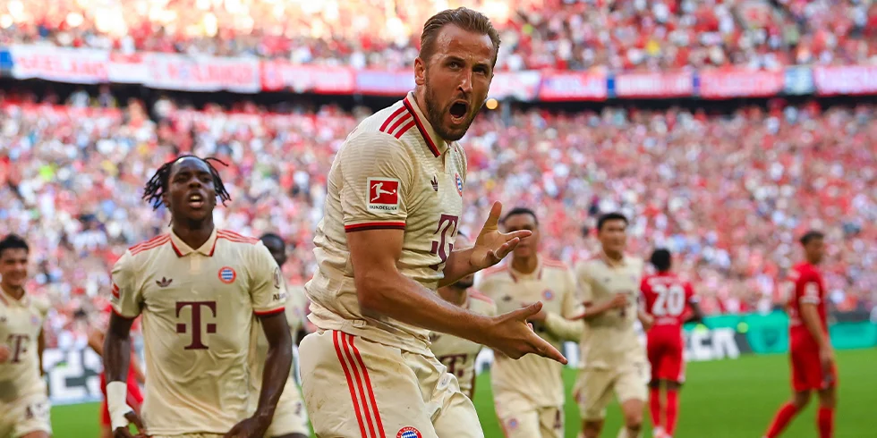 Harry Kane bejubelt ein Tor im weißen FC Bayern München Trikot, mit offenem Mund und Fingerguns. (Foto)