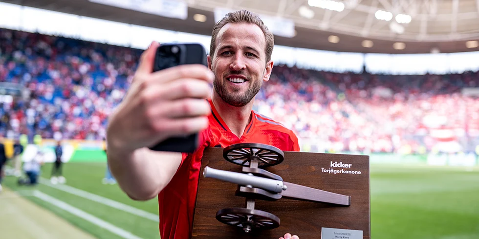 Harry Kane vom FC Bayern München strahlt mit der 'kicker' Torjägerkanone Trophäe in der Hand und zu ihm gedrehtes iPhone in der anderen – ein typischer „neuer Rekord, erstmal ein Foto“-Moment. (Foto)