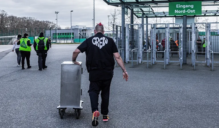 Ein Mann mit dem Aufdruck „Crew“ schiebt einen silbernen Kasten. (Foto)