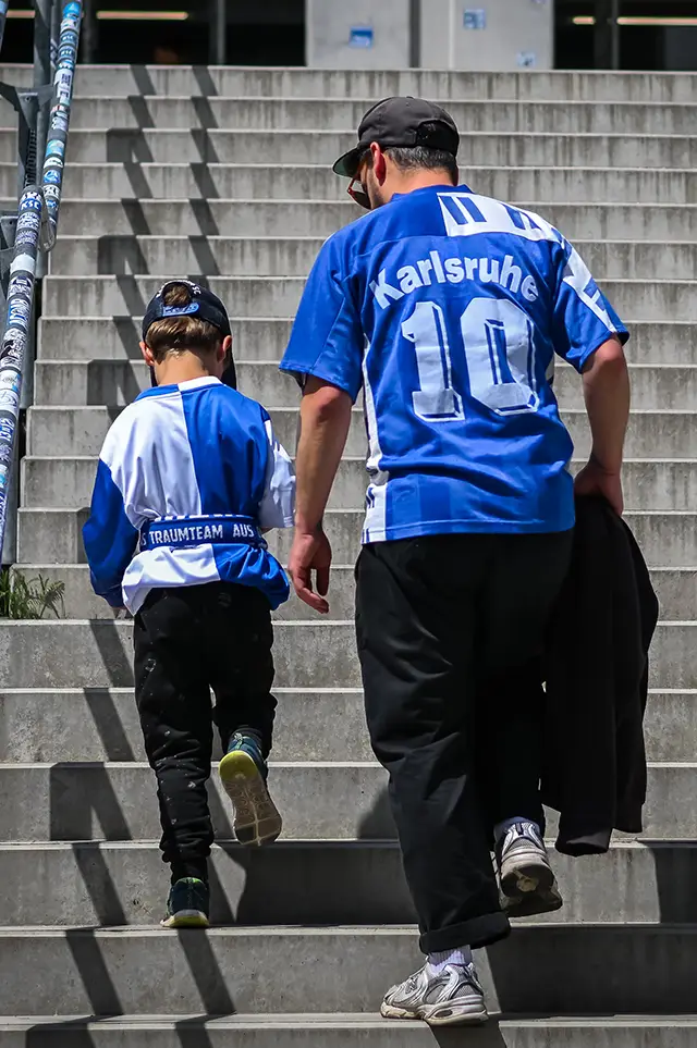 Ein Fan des KSC begleitet seine Tochter in ein Stadion. Beide tragen ein KSC Trikot. (Foto)