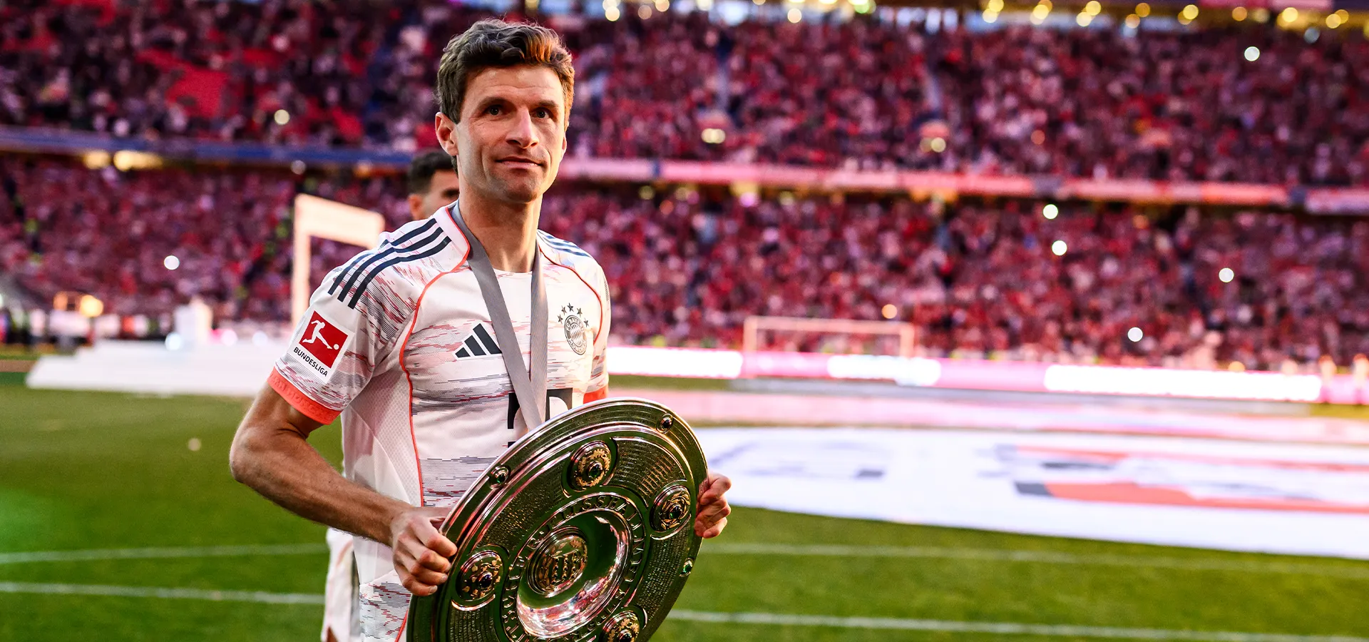 Thomas Müller hält die Bundesliga-Meisterschale in Händen und grinst in die Kamera (Foto)