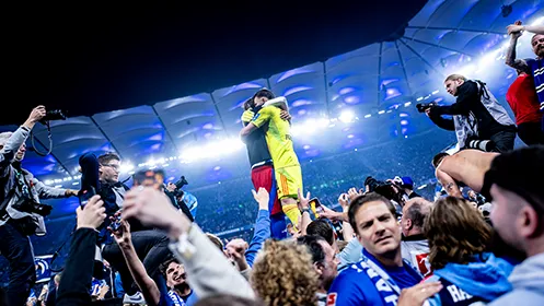 The HSV goalkeeper and another player embrace on the pitch after promotion. (Photo)